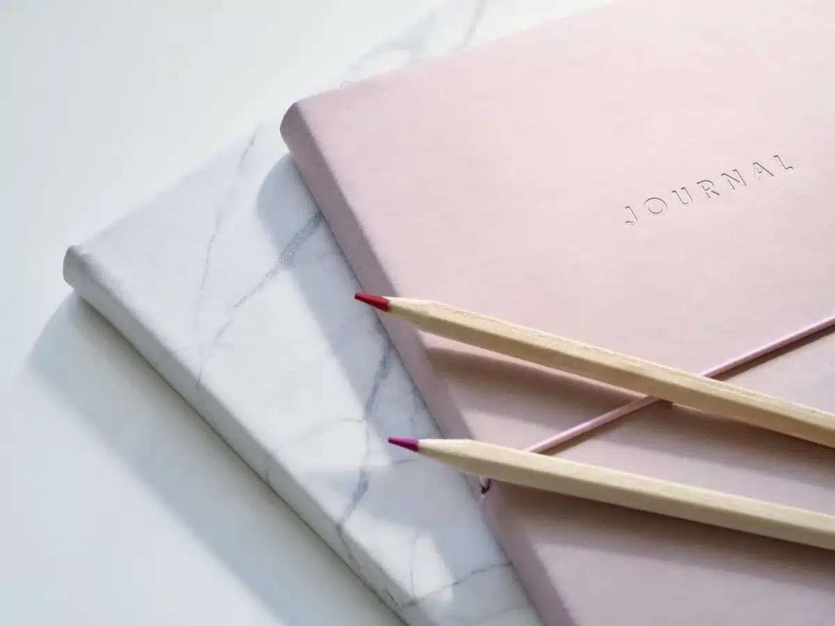 Personne écrivant dans un carnet avec une bougie rose à côté, lumière du jour